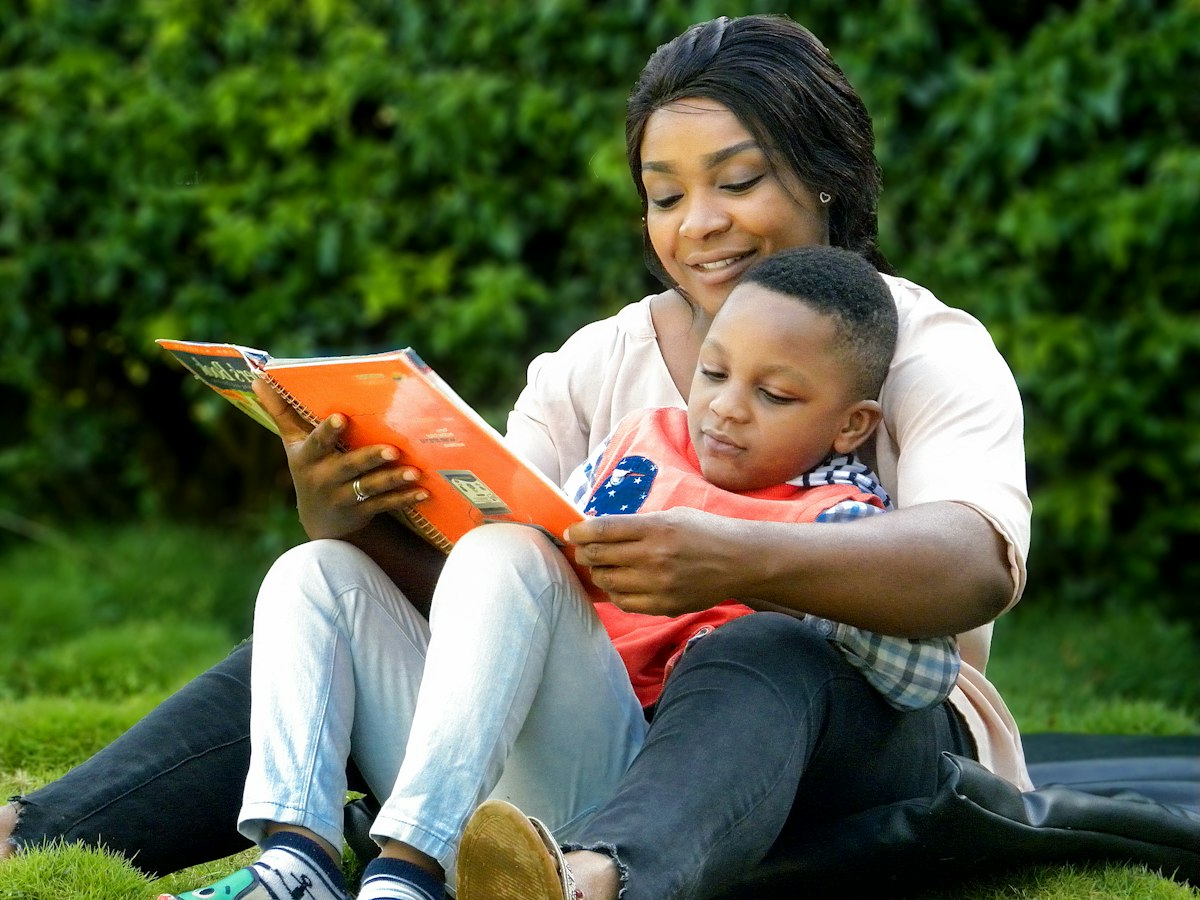 A mother and child sharing a book outdoors.